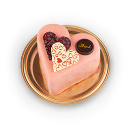 Ein herzförmiger rosa Kuchen steht auf einem goldenen Tablett, gekrönt von drei dekorativen Schokoladenherzen in Rot, Weiß und Braun mit Herzmustern und einer kleinen runden Schokolade mit der Aufschrift Inook.