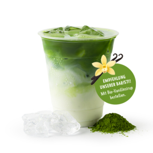 Ein Plastikbecher, gefüllt mit einem eisgekühlten Matcha-Latte, dessen Inhalt sich in grüne und weiße Schichten unterteilt. Neben dem Becher liegen Eiswürfel und ein Häufchen Matcha-Pulver. Auf einem Aufkleber ist eine Vanilleblüte abgebildet, und es wird auf Deutsch empfohlen, Bio-Vanillesirup hinzuzufügen.