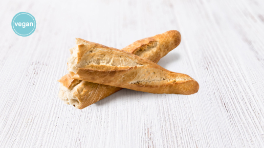 Zwei knusprige Baguettes auf einer weißen Holzunterlage mit einem blauen veganen Etikett in der oberen linken Ecke.