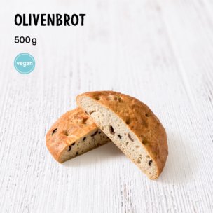 Ein rundes Olivenbrot, halbiert, auf einer weißen Holzunterlage, mit der Aufschrift „OLIVENBROT 500 g“ und einem blauen Vegan-Symbol. Im Inneren des Brotes sind Olivenstücke zu erkennen.