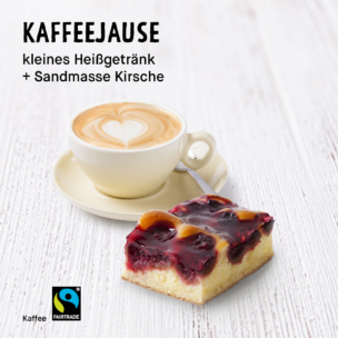 Auf einer weißen Holzplatte steht eine Tasse Kaffee mit herzförmiger Latte-Art neben einem Stück Biskuitkuchen mit Kirschen. Der Text lautet: KAFFEEJAUSE kleines Heißgetränk + Sandmasse Kirsche. Das Fairtrade-Logo ist zu sehen.