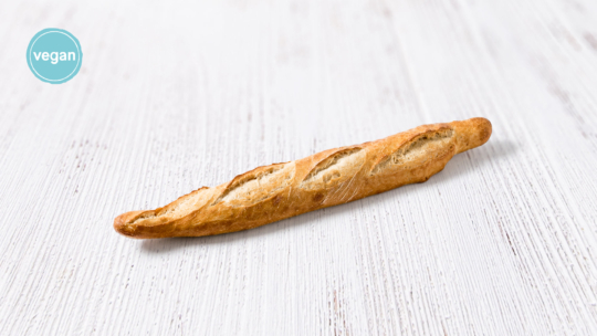 Ein goldbraunes Baguette auf einer weißen Holzunterlage mit einem blauen veganen Etikett in der Ecke.
