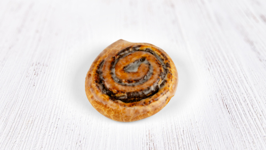 Auf einer weißen Holzfläche liegt eine einzelne, glasierte Zimtschnecke in Spiralform.