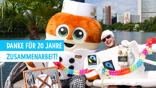 Eine lächelnde Person und ein großes Brötchen-Maskottchen feiern auf einem Boot mit bunten Dekorationen, einem Fairtrade-Schild und Besteck neben einem See. Der Text auf Deutsch lautet: „Danke für 20 Jahre Zusammenarbeit!“.